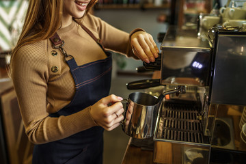 Cropped photo, young girl, barista steaming milk at the modern coffee shop