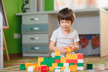 Children play with a toy designer on the floor of the children's room. Boy playing with colorful blocks. Kindergarten educational games.