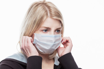  A close-up of an adult white woman wearing and adjusting a disposable mask on her face. On a white...
