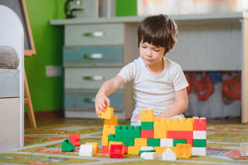 Child playing with colorful toy blocks. Little boy building tower at home or day care. Educational toys for young children. Construction block for baby or toddler kid. Mess in kindergarten play room.