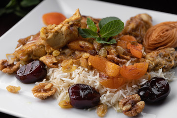 Chyhyrtma pilaf with lamb meat, dried fruits, dates and walnuts, on a white plate