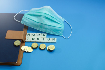 Surgical face mask with block letters and coins with a notebook on a blue background.  Business and...