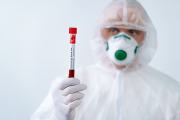 Positive COVID-19 test. Virologist in a medical mask and protective suit holds a test tube with positive blood sample