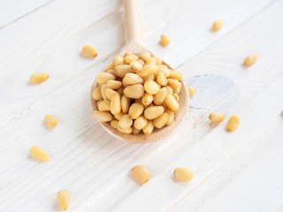 Peeled pine nuts in wooden spoon on white textured background. Unshelled kernels. Superfood, vegan, vegetarian food concept. Selective focus. Healthy snack.