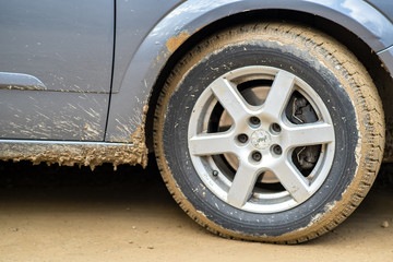 Close up of dirty car wheel with rubber tire covered with yellow mud.