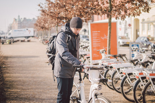 Man Taking Bike In Bike Sharing. Man Take City Bicycle Vacation At The Parking. Public Electric Bikes For Rent Parked In Copenhagen, Denmark. Save CO2 And Green Energy. Person And Cycle In Europe