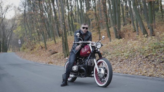 Portrait of brutal biker in sunglasses and leather on motorcycle on roadway