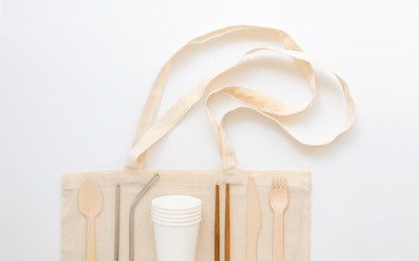 Set of eco-friendly reusable dish and metal drinking cups on a straw bag. Flat lay zero waste concept on a white background
