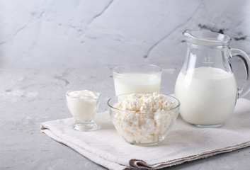 Dairy products: milk, kefir or ayran, cottage cheese and sour cream in a transparent bowl, jug and glass on a gray background, space for text, Closeup