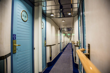 A long corridor in blue style with cabin doors on the deck of a modern passenger ferry