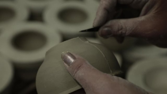Workshop. Women's hands are stroking the clay Cup, cleaning the roughness with a stick. Grayscale. Close up.