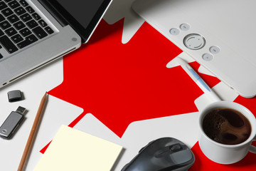 Canada national flag on top view work space of creative designer with laptop, computer keyboard, usb drive, graphic tablet, coffee cup, mouse on wooden table.