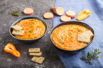 Sweet potato or batata cream soup with sesame seeds and snacks in blue ceramic bowls on a black concrete background. side view, close up.