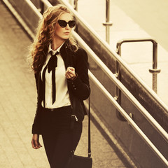 Young fashion business woman in sunglasses walking on city street
