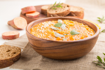 Sweet potato or batata cream soup with sesame seeds in a wooden bowl on a white wooden background. side view, selective focus.