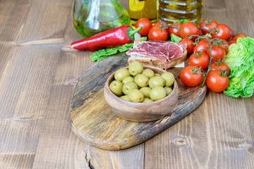 Light healthy food with vitamins and minerals background. Kitchen wooden table. Green olives, sandwitch with jamon, vegatables and olive oil bottles.