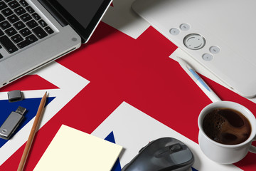 United Kingdom national flag on top view work space of creative designer with laptop, computer keyboard, usb drive, graphic tablet, coffee cup, mouse on wooden table.
