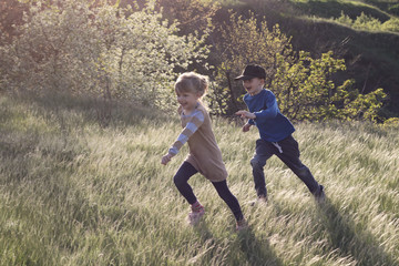 Fototapeta premium Little happy children run and play in the tall beautiful grass.