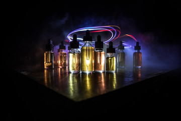 Smoke clouds and vape liquid bottles on dark background. Light effects. Useful as background or...