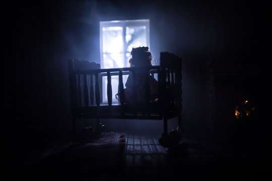 Old creepy eerie baby crib near window in dark room. Scary baby silhouette in dark. A realistic dollhouse living room with furniture and window at night