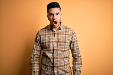 Young handsome man wearing casual shirt standing over isolated yellow background afraid and shocked with surprise and amazed expression, fear and excited face.