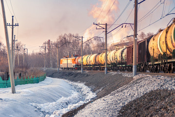 freight train leaving a bend, trees behind an industrial area, winter evening