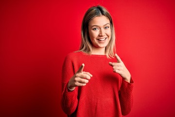 Young beautiful blonde woman wearing casual sweater over red isolated background pointing fingers to camera with happy and funny face. Good energy and vibes.