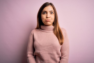 Fototapeta premium Beautiful young woman wearing turtleneck sweater over pink isolated background puffing cheeks with funny face. Mouth inflated with air, crazy expression.