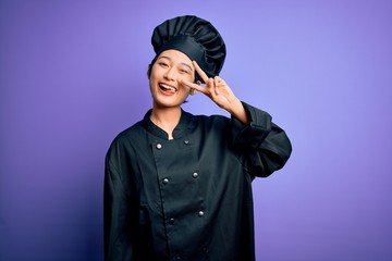 Young beautiful chinese chef woman wearing cooker uniform and hat over purple background Doing peace symbol with fingers over face, smiling cheerful showing victory