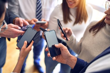 Group of business workers standing with hands together using smartphone doing symbol at the office