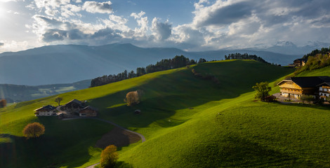 Aerial view of improbable green meadows of Italian Alps, green slopes of the mountains, Bolzano, huge clouds over a valley, roof tops of houses, Dolomites on background, sunshines through clouds © Vladimir Drozdin