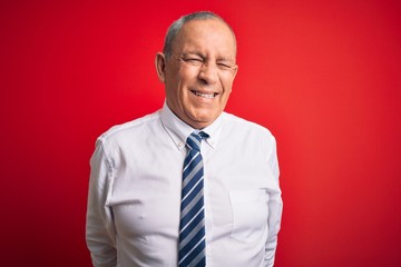 Senior handsome businessman wearing elegant tie standing over isolated red background winking looking at the camera with sexy expression, cheerful and happy face.