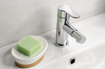 Soap in a soap dish on a white sink in the bathroom next to a chrome faucet.