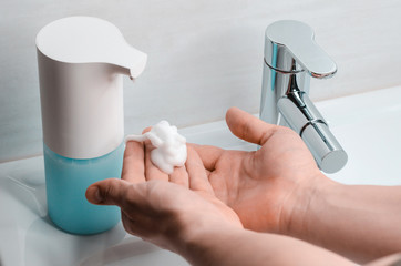 Automatic soap dispenser in the bathroom. Hands with soapy solution close-up. The fight against coronavirus.