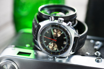 Vintage pilot chronograph watch, with black leather strap laying on film photo camera in green...