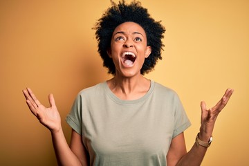 Young beautiful African American afro woman with curly hair wearing casual t-shirt crazy and mad...
