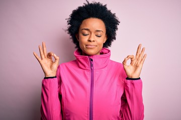 Young African American afro sportswoman with curly hair wearing sportswear doin sport relax and smiling with eyes closed doing meditation gesture with fingers. Yoga concept.