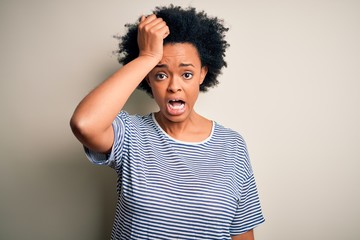 Fototapeta na wymiar Young beautiful African American afro woman with curly hair wearing striped t-shirt surprised with hand on head for mistake, remember error. Forgot, bad memory concept.