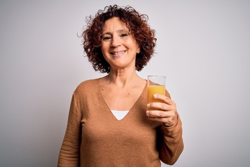 Middle age curly hair woman drinking healthy glass of orange juice over white background with a happy face standing and smiling with a confident smile showing teeth