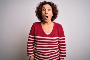 Middle age beautiful curly hair woman wearing casual striped sweater over white background afraid and shocked with surprise expression, fear and excited face.
