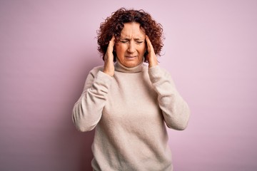 Middle age beautiful curly hair woman wearing casual turtleneck sweater over pink background with hand on headache because stress. Suffering migraine.