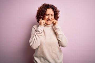 Middle age beautiful curly hair woman wearing casual turtleneck sweater over pink background covering ears with fingers with annoyed expression for the noise of loud music. Deaf concept.