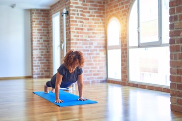 Middle age beautiful sportwoman standing on mat. Practicing yoga doing downward-facing dog pose at...