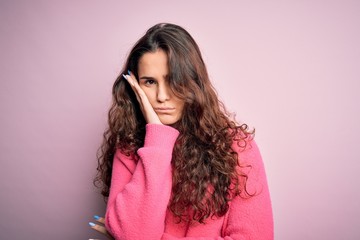 Young beautiful woman with curly hair wearing casual sweater over isolated pink background thinking looking tired and bored with depression problems with crossed arms.