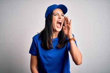 Young delivery woman with blue eyes wearing cap standing over blue background shouting and screaming loud to side with hand on mouth. Communication concept.