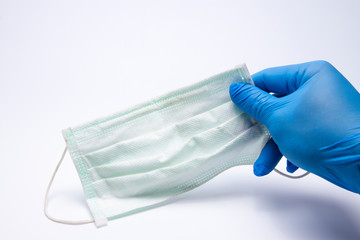 First-person perspective, wearing to a medical blue hand, holding a face mask above the white surface table background Respirator mask for spreading the virus up close,used mask