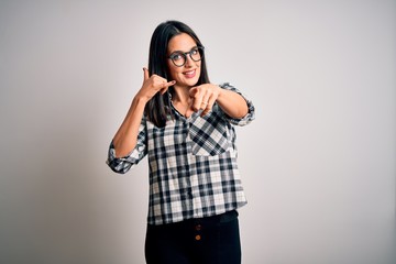 Young brunette woman with blue eyes wearing casual shirt and glasses over white background smiling doing talking on the telephone gesture and pointing to you. Call me.