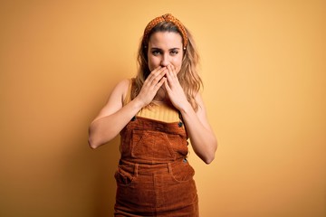 Young beautiful blonde woman wearing overalls and diadem standing over yellow background laughing...
