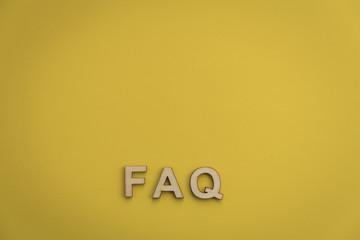 FAQ wood letters searching for facts truth news answers concept copy space flat lay on muted yellow