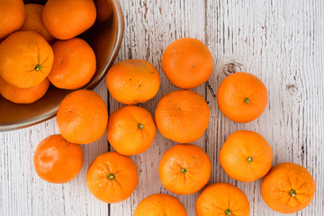 Small clementine oranges spilling out of a stainless-steel bowl on a whitewashed wood background
